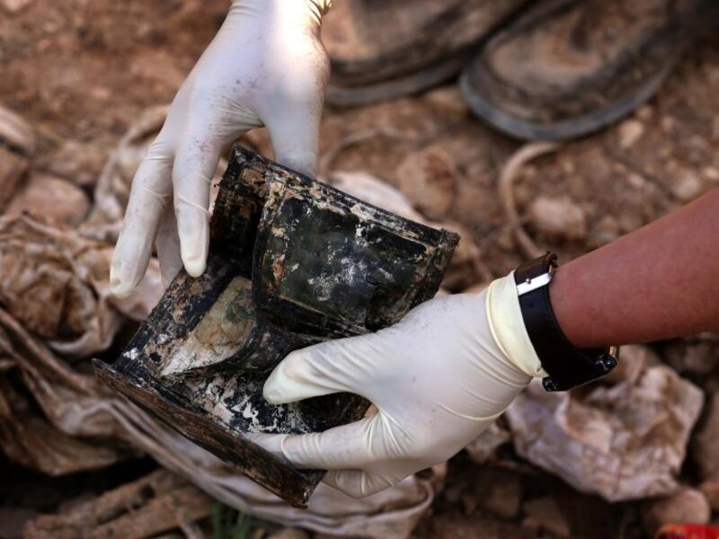 a member of the Yazidi minority searches in a wallet for clues, that might lead him to missing relatives in the remains of people killed by the Islamic State. (Safin HAMED / AFP)