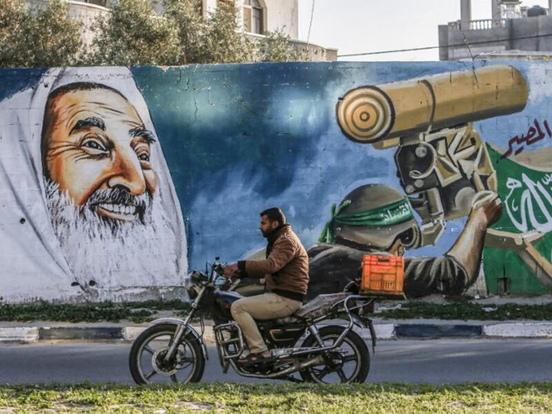 A Palestinian drives a motorcycle past a mural depicting late Hamas spiritual leader Sheikh Ahmed Yassin and a masked fighter of the Qassam Brigades, the armed wing of the Hamas movement, manning a turret alongside a street in Rafah in the southern Gaza Strip 
SAID KHATIB / AFP