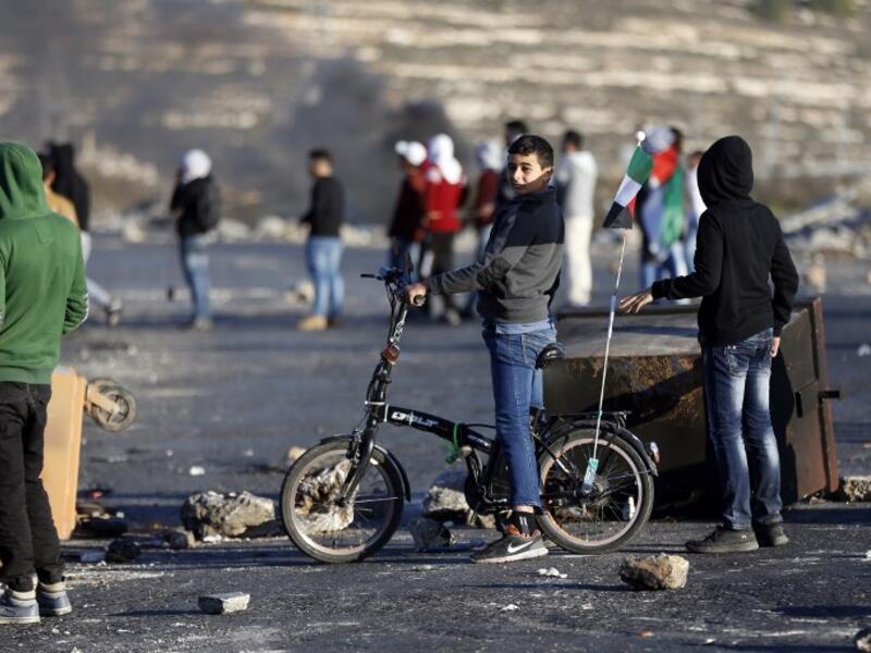 A Palestinian boy rides his bike during clashes with Israeli forces near an Israeli checkpoint in the West Bank city of Ramallah.
(ABBAS MOMANI / AFP)