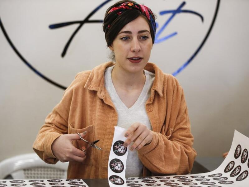 Amira Khader (L), Palestinian creative director of the feminist fashion label "BabyFist", cuts stickers while founder Yasmeen Mjalli stands next to her in their shop in Ramallah 
ABBAS MOMANI / AFP