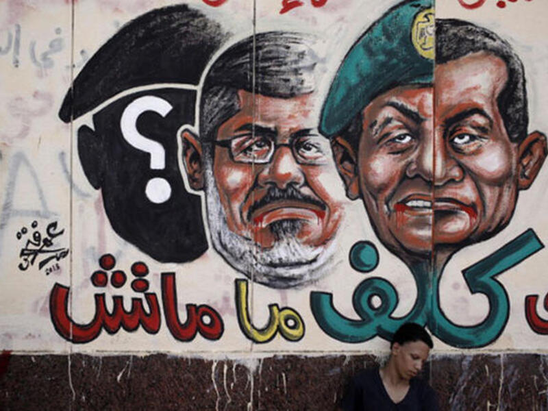 An opposition demonstrator sits below graffiti of Egyptian President Morsi on the walls of Egypt's Presidential Palace in Cairo, Egypt. (Image: by Ed Giles/Getty Images)