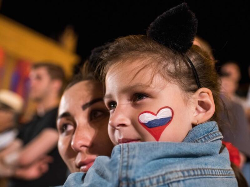A woman holds a girl with a Russian flag shaped as a heart, painted on her left cheek as they watch the Russia 2018 World Cup Group D football match between Croatia and Nigeria on a giant screen at the official FIFA Fan Fest in Volgograd on June 16, 2018. 
NICOLAS ASFOURI / AFP