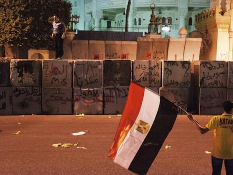 A protester stands on top of the Presidential Palace defensive walls as an other holds a national flag (AFP)