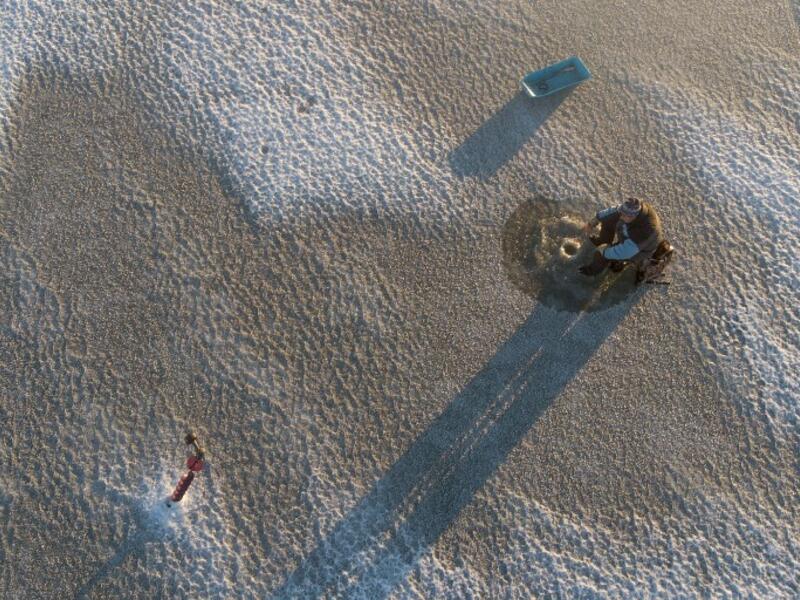 An aerial view shows a man sitting near a hole drilled into the frozen sea using an auger (L), as he ice fishes on the Gulf of Bothnia, near Vaasa, Western Finland on December 28, 2018, where winter daylight last for some four hours. 
Olivier MORIN / AFP