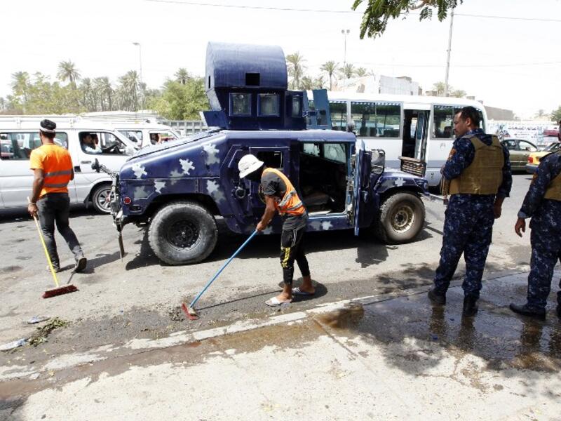 Iraqi workers clean the pavement as security forces stand guard at the site of a suicide bombing on July 24, 2016 near a checkpoint in the Kadhimiyah area, home to a major Shia shrine, in northern Baghdad. (AFP/Sabah Arar)