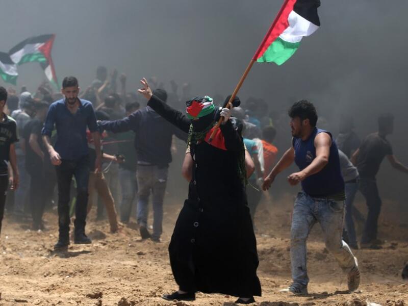 A Palestinian woman waves her national flag during clashes with Israeli forces near the border between Israel and the Gaza Strip, east of Jabalia on May 14, 2018, as Palestinians protest over the inauguration of the US embassy following its controversial move to Jerusalem. MOHAMMED ABED / AFP