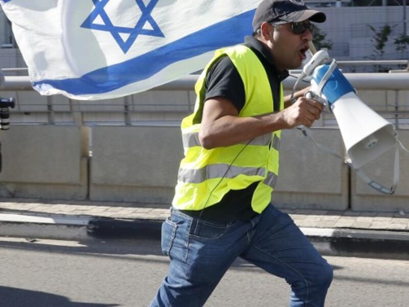 An Israeli protester wearing a yellow vest and carrying a national flag use a loudspeaker to shout slogans during demonstrations against the rising cost of living on December 14, 2018.
JACK GUEZ / AFP