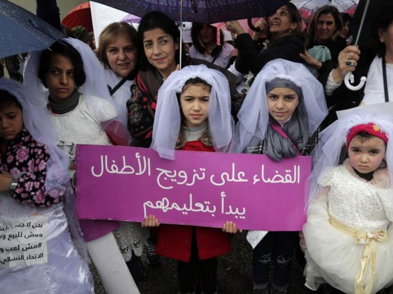 Young Lebanese girls disguised as brides hold a placard as they participate in a march against marriage before the age of 18, in the capital Beirut on March 2, 2019. The placard in Arabic reads "The end of child marriage begins by educating them". 
ANWAR AMRO / AFP