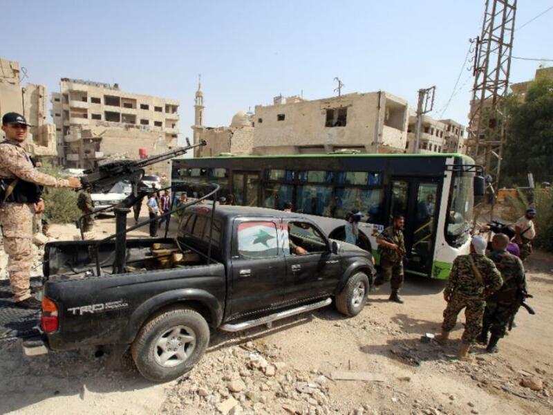 Syrian government troops stand guard as a bus carrying people drives by, as part of an evacuation from the town of Daraya outside the capital Damascus on August 26, 2016. (AFP/Youssef Karwashan)