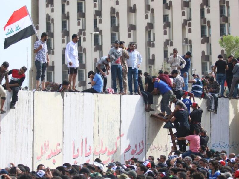 Iraqi protesters climb over a concrete wall surrounding the parliament after breaking into Baghdad. (AFP/File)