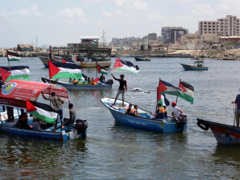 Palestinians hold their national flag as they ride boats during a rally to show support for activists aboard the flotilla. (AFP/Mahmud Hams)