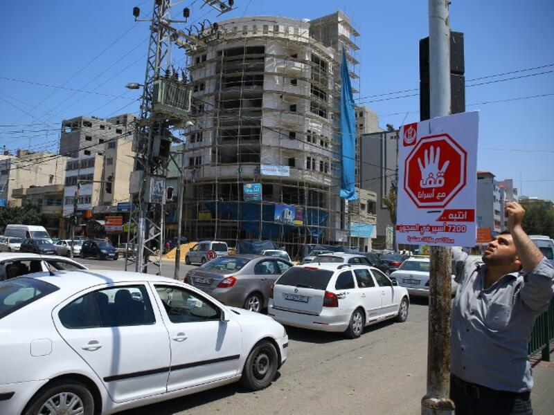A Palestinian man hangs on May 22, 2017 in Gaza City a traffic sing with Arabic writing on reading "stand with our prisoners'' in solidarity with Palestinian hunger-striking prisoners in Israeli jails. (AFP/Mohammed Abed)