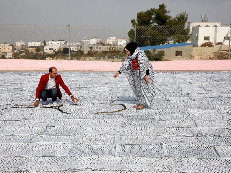 Palestinian Southern Education Direction's member Safa'a Amro (R) prepares a one thousand four hundred Meter square Keffiyeh. (HAZEM BADER / AFP)