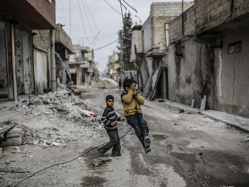 Children swing on an electrical wire hanging off a damaged building in Kobani. After the liberalization from Daesh in 2015, many people have returned to the city. Yet, reconstruction has been made difficult by the closure of border crossings with Turkey that prevented the importation of goods such as cement, iron, medicines, food and technology.