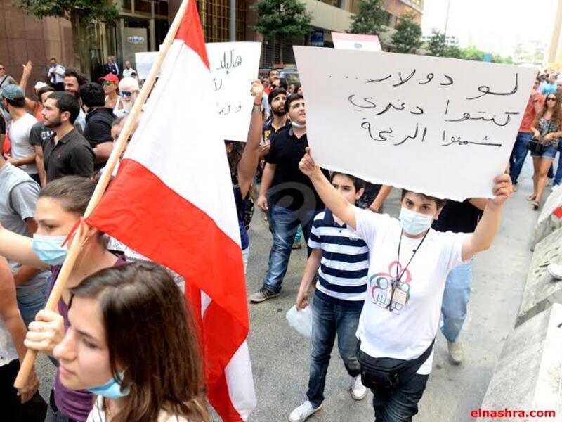 متظاهر يضع كمامة بسبب ريحة القمامة ويحمل شعار "لو دولار كنتوا دغري شميتوا الريحة" واصفاً أن المسؤوليين لم يهتموا برائحة القمامة ولو هناك فائدة مادية لكانوا تحركوا.