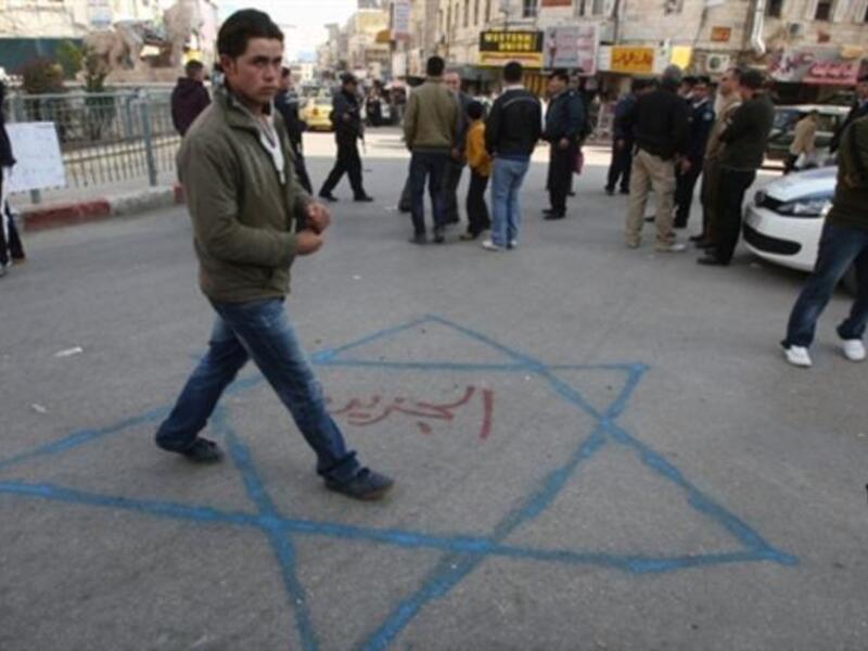 A Palestinian youth walks on a Star of David sprayed on the ground with Al-Jazeera written in red Arabic letters in the middle during a demonstration in the West Bank city of Ramallah.