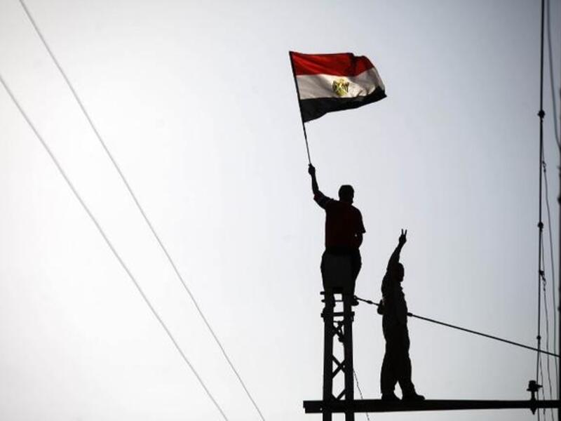 Protestor waves a flag as another makes the victory sign at the top of a Cairo electricity pole (AFP)