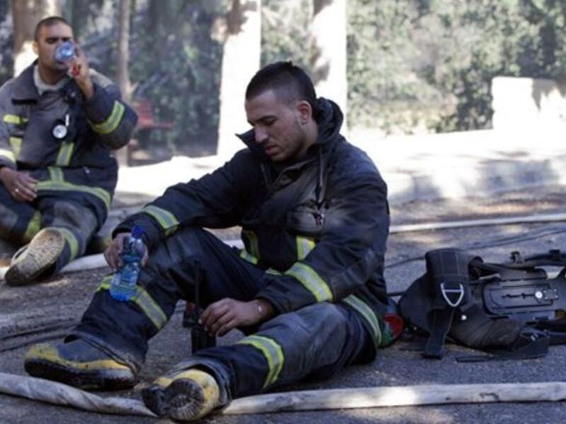 Israeli firefighters take a break after dousing flames in the village of Ein Hod.