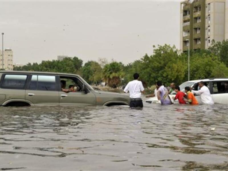 Saudi men are trying to push a car stuck in a flooded street.