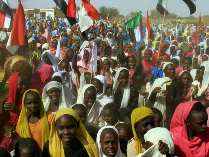 Sudanese women wave their national flag as they wait for the arrival of special envoys in the Shangil Tobaya area for displaced people in North Darfur state (AFP)