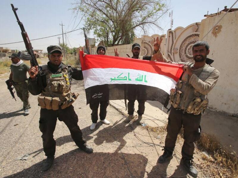 Members of Iraq's mainly Shiite Popular Mobilization Units hold up an Iraqi flag.  The volunteer militia, though split into several factions, has been instrumental in the fight against Daesh militants in Iraq.  (AFP/File).  