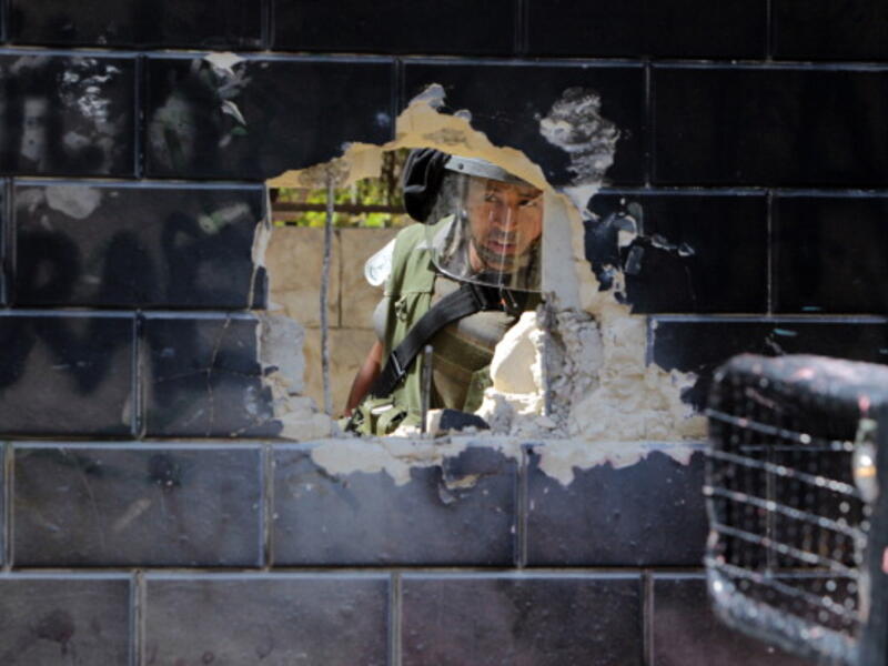 Israeli security guard peering through a hole of Israel's  separation barrier by Palestinian youth in the Abu Dis neighrbood, bordering Jerusalem on July 9, 2013. [Abbas Momani/Getty Images]
