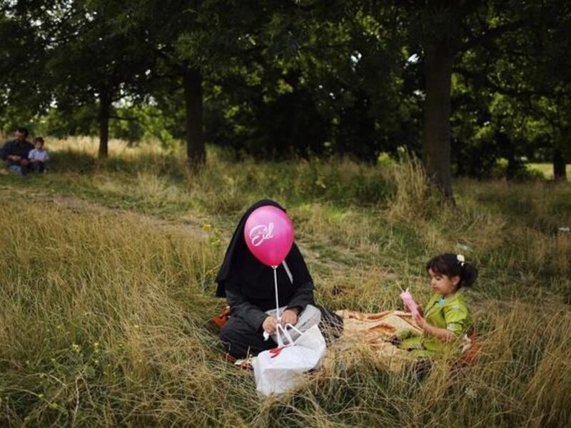A woman and girl sit in the shade in Burgess Park during an Eid celebration fun fair in London, England. (GETTY)