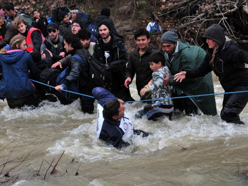 Migrants and refugees cross a river on their way to Macedonia from a makeshift camp at the Greek-Macedonian border on March 14, 2016, where thousands are stranded by the Balkan border blockade. (AFP/Sakis Mitrolidis)