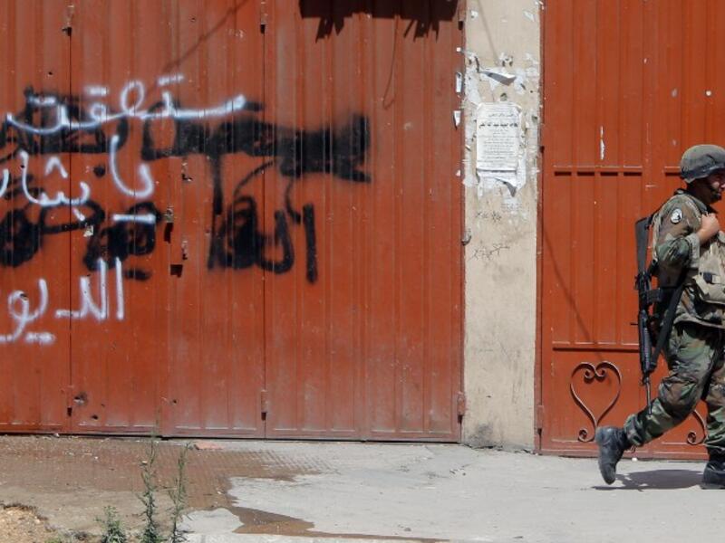  A Lebanese army soldier walks past graffiti on a closed shop which reads: "You shall fall Bashar.." in Tripoli's Sunni neighbourhood of Bab al-Tabbaneh, whose residents support the rebels battling to topple the regime in nearby Syria, during a truce with the Alawite district of Jabal Mohsen on May 27 (Joseph Eid/ AFP)