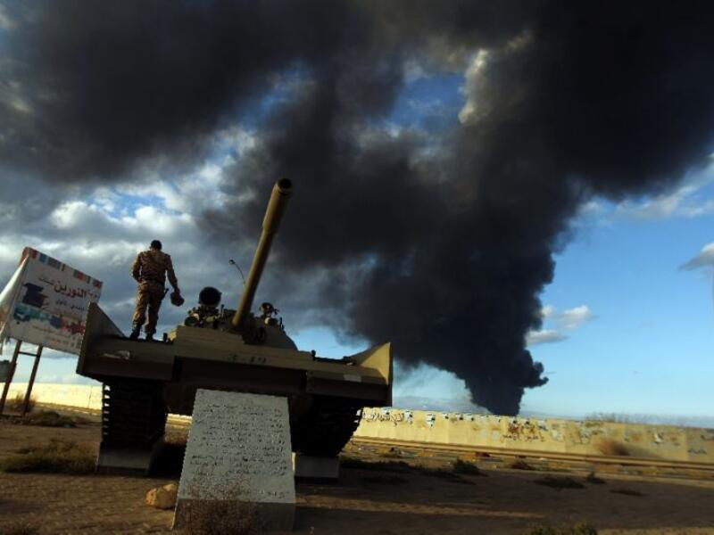 A member of the Libyan army stands on a tank as heavy black smoke rises from the city's port during clashes in the eastern Libyan city of Benghazi on December 23, 2014. (AFP Photo/Abdullah Doma)