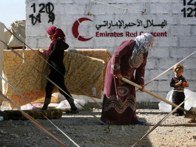Syrian-Kurdish refugees work near tents erected by the United Arab Emirate's Red Crescent as aid is distributed at the Qushtapa refugee camp, 15 kilometers South of Arbil. [AFP]
