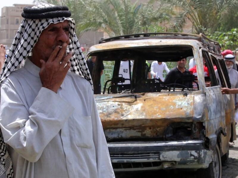 An Iraqi man smokes a cigarette in front of a burnt vehicle at the site of a car bombing at a market in Baghdad's impoverished district of Sadr City. AFP Photo