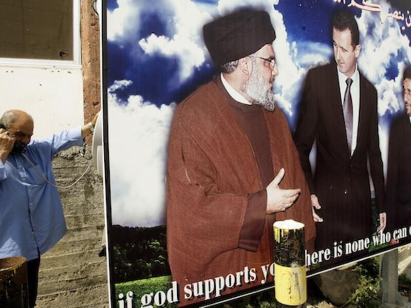  A Lebanese man uses a public phone near a poster featuring Syrian President Bashar Assad, Hezbollah chief Hassan Nasrallah and Iran president Mahmoud Ahmadinejad last week in the southern Lebanese city of Naqura. AFP Photo