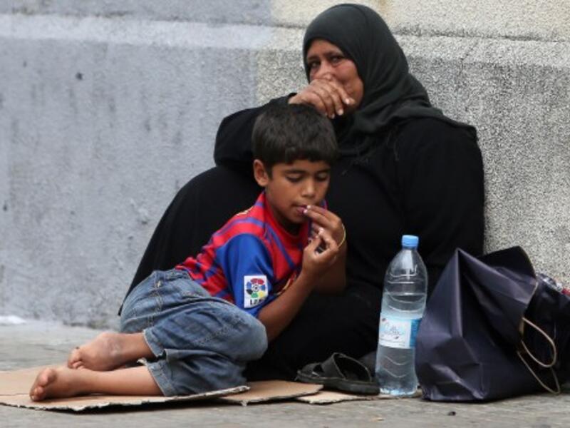 A Syrian refugee boy sits with his mother as they beg on the sidewalk in Beirut (AFP)