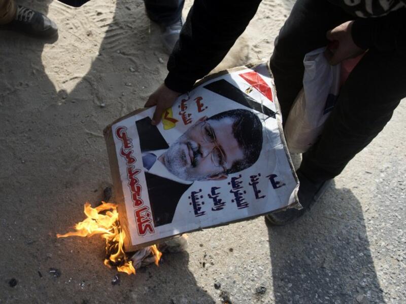 An opponent to the Muslim Brotherhood set fire to a portrait of ousted president Mohamed Morsi during a demonstration outside the Cairo police academy where his trial was set to take place before it was postponed until Feb. 1, 2014. (AFP)
