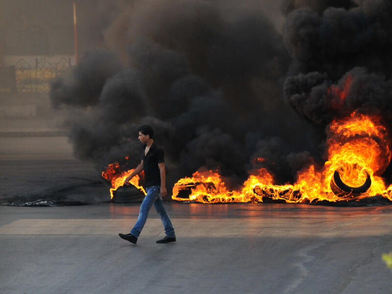 LEBANON, Tripoli : A youth walks past burning tires across a street in the northern city of Tripoli, on June 23, 2013, during protests in support of Sunni Muslim Sheikh Ahmad al-Assir whose supporters have clashed with the Lebanese army in the southern Lebanese city of Sidon. (Credit: AFP)