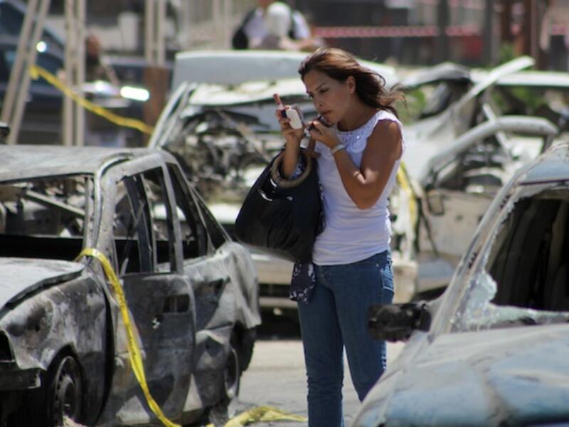 A Lebanese woman puts on make-up near vehicles that were damaged in a bombing outside Al-Taqwa mosque on August 24, 2013 in the northern city of Tripoli. (AFP)