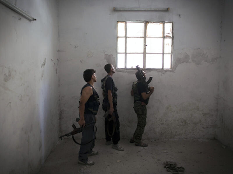 Rebel fighters look at the pro-government forces' positions through a window as they hold a position in an empty room in the Salaheddine district of the northern Syrian city of Aleppo, on July 9, 2013. (Source: AFP/JM LOPEZ)