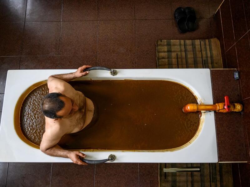 A man bathes in a tub filled with Naftalan crude oil during a treatment session at Sehirli Naftalan Health Center, some 300 kilometres (186 miles) from capital Baku, on March 21, 2019. Immersed up to her neck in crude oil, a Russian woman suffering from joint disease smiles in delight, confident that the treatment at a spa in northwestern Azerbaijan will cure her painful condition.  Mladen ANTONOV / AFP
