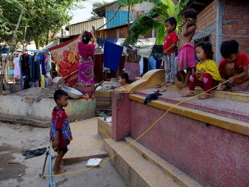 This picture shows children playing on a grave as a woman dries her clothes on another grave in Phnom Penh.  TANG CHHIN Sothy / AFP