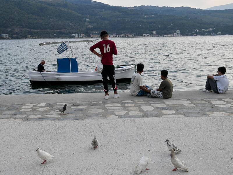 Migrant youth sit by a local fisherman at the city of Vathy on the island of Samos.  LOUISA GOULIAMAKI / AFP