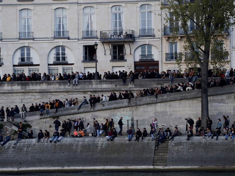 People look at the fire engulfing the Notre-Dame Cathedral in central Paris from the quai de la Tournelle on the banks of the Seine river on April 15, 2019. Geoffroy VAN DER HASSELT / AFP