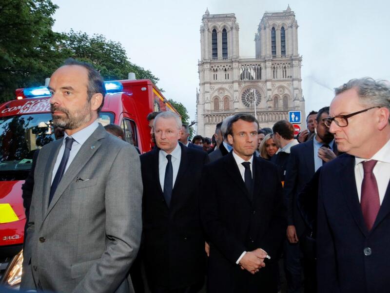 French Prime Minister Edouard Philippe (L), and French President Emmanuel Macron (3rd L) gather near the entrance of the Notre-Dame de Paris Cathedral in Paris, as flames engulf its roof on April 15, 2019. PHILIPPE WOJAZER / POOL / AFP