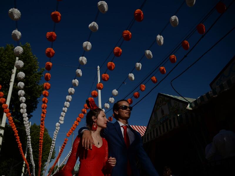 A couple walks past "casetas" (stalls) during the "Feria de Abril" (April Fair) festival in Seville on May 6, 2019. The fair dates back to 1847 when it was originally organized as a livestock fair but has turned into a week of flamenco dancing, music and bullfighting.  CRISTINA QUICLER / AFP