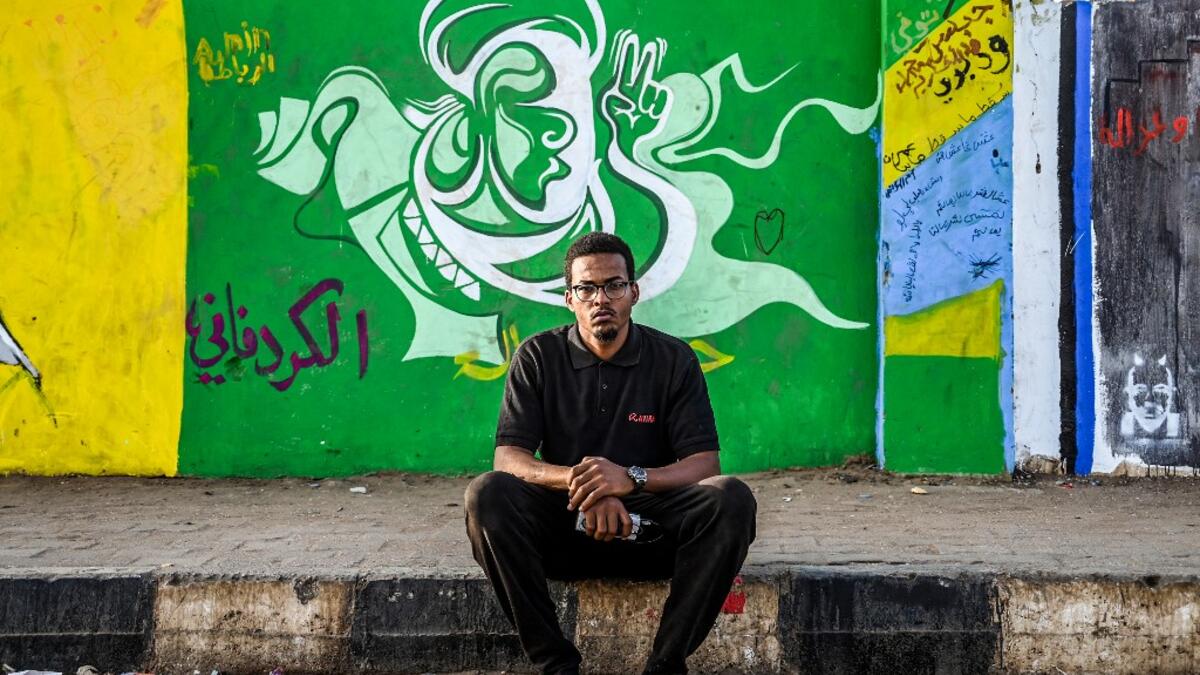 Sudanese graffiti artist Belal Abdelrahaman sits in front of a recently painted mural made by his team during a protest near the army headquarters in the capital Khartoum  OZAN KOSE / AFP