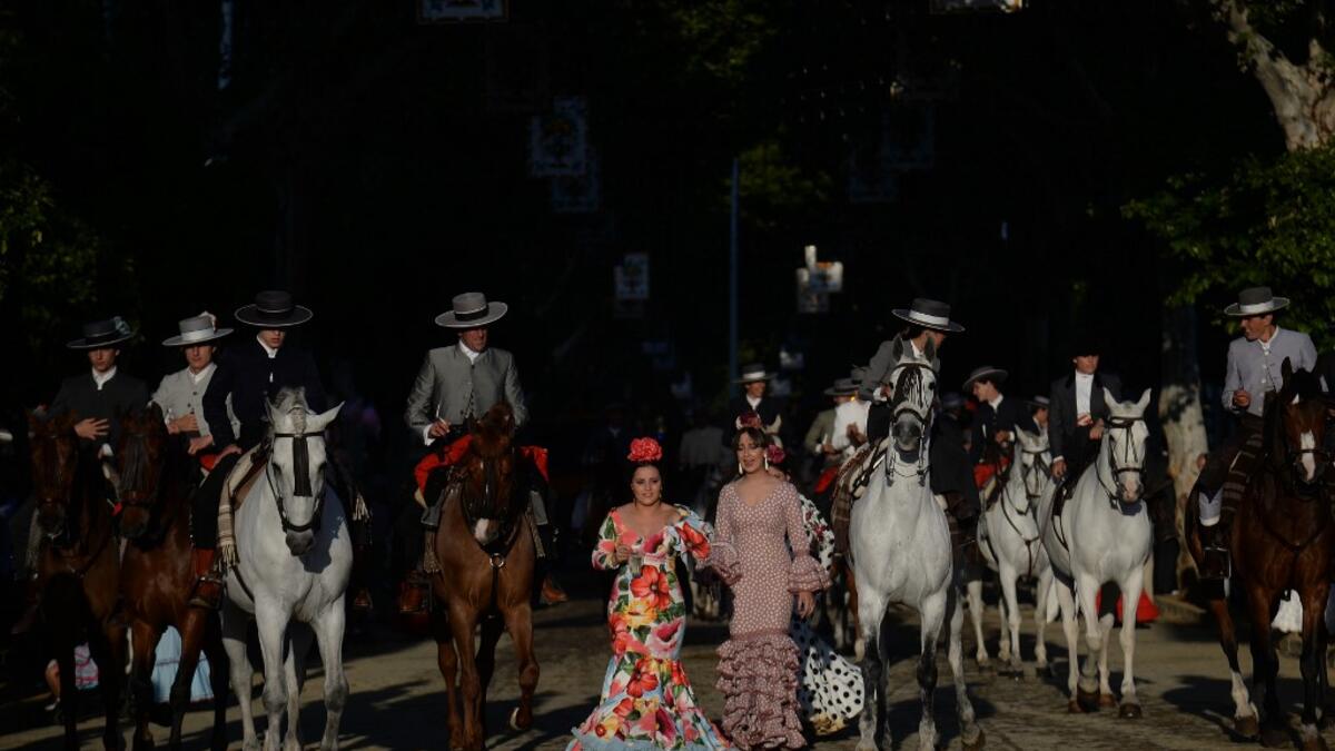 People in traditional Sevillian costumes ride horses and walk along the street during the "Feria de Abril" (April Fair) festival in Seville on May 6, 2019. CRISTINA QUICLER / AFP