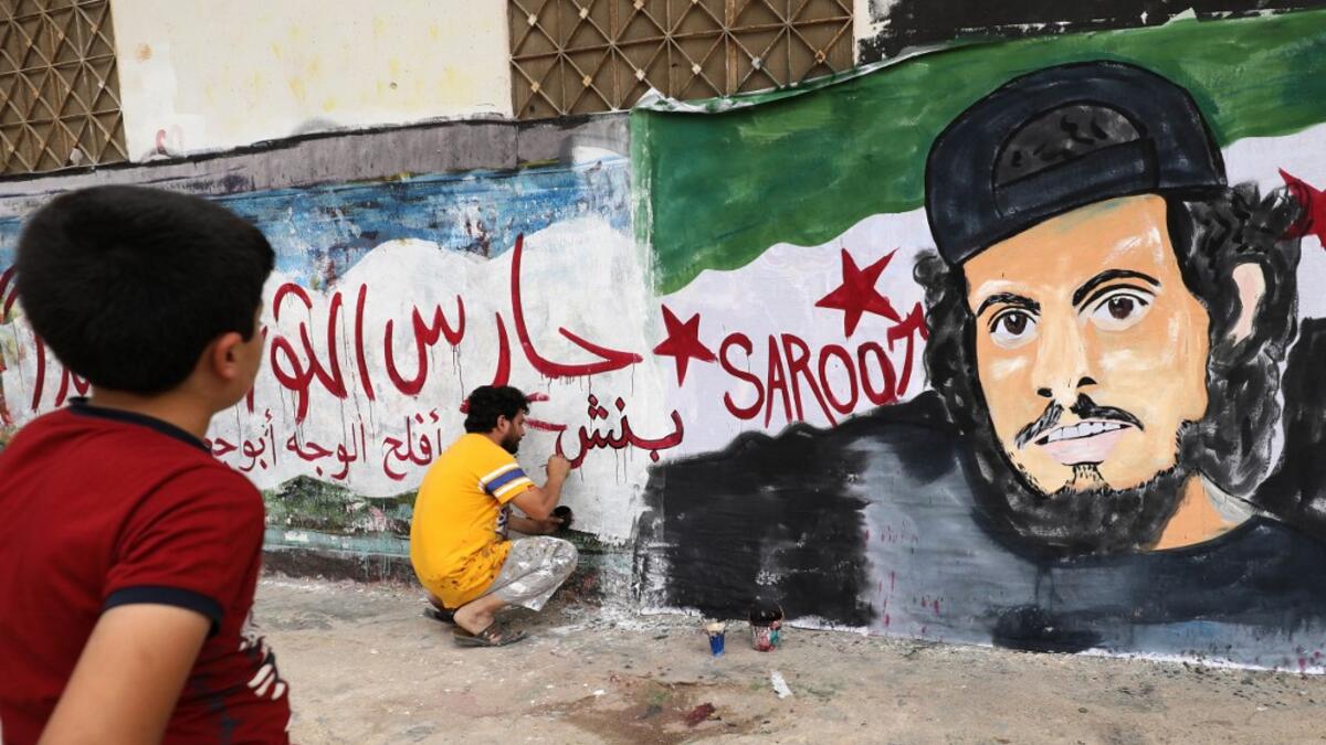 A child watches as a local artist works on a mural painting showing the late Syrian rebel fighter Abdel-Basset al-Sarout in the town of Binnish in the jihadist-held northern Idlib province on June 8, 2019. OMAR HAJ KADOUR / AFP