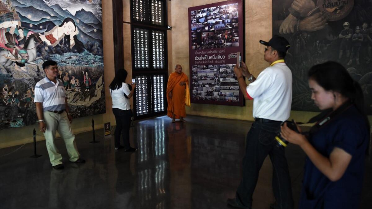 This picture taken on June 13, 2019 shows visitors taking photos in front of artwork illustrating the rescue of the 12 boys from the "Wild Boars" football team and their coach, who were trapped in the Tham Luang cave last year, at the cave's visitor centre in the Mae Sai district of Chiang Rai province. Lillian SUWANRUMPHA / AFP