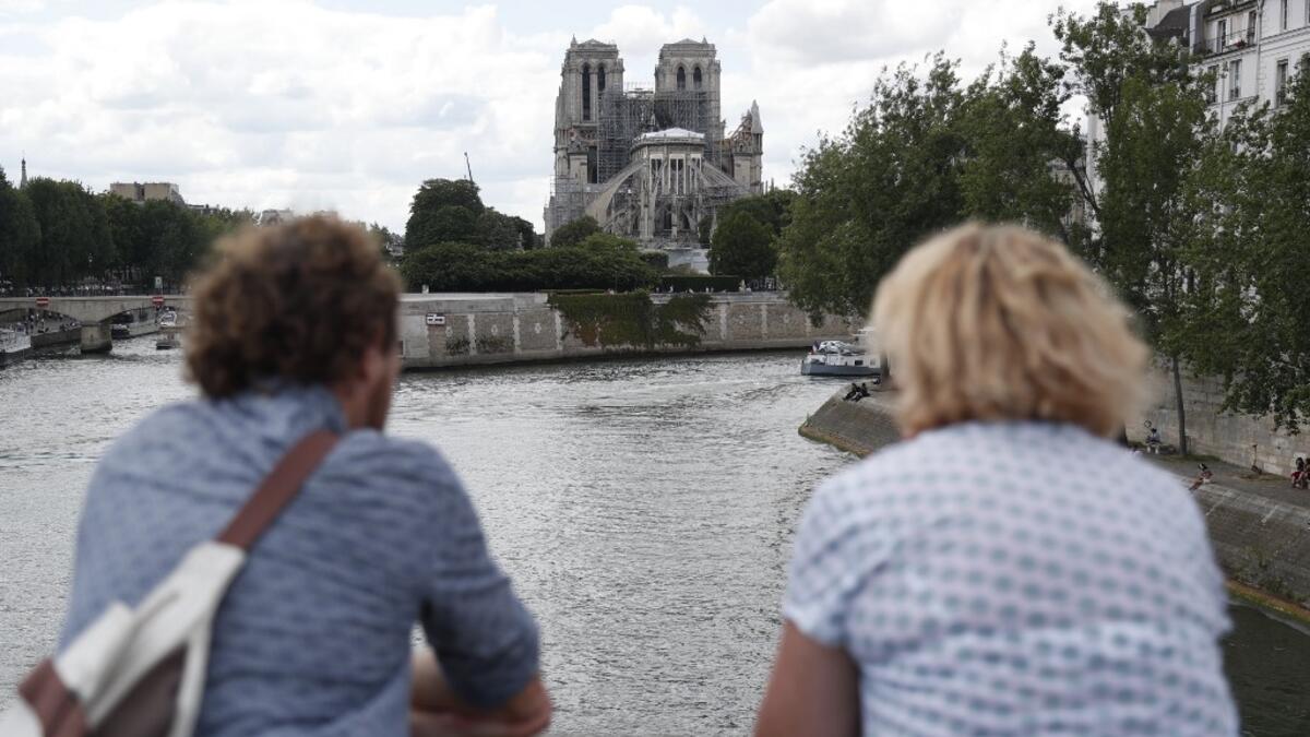 People stand on the river bank as they look towards the Notre-Dame de Paris cathedral on June 15, 2019. Zakaria ABDELKAFI / AFP