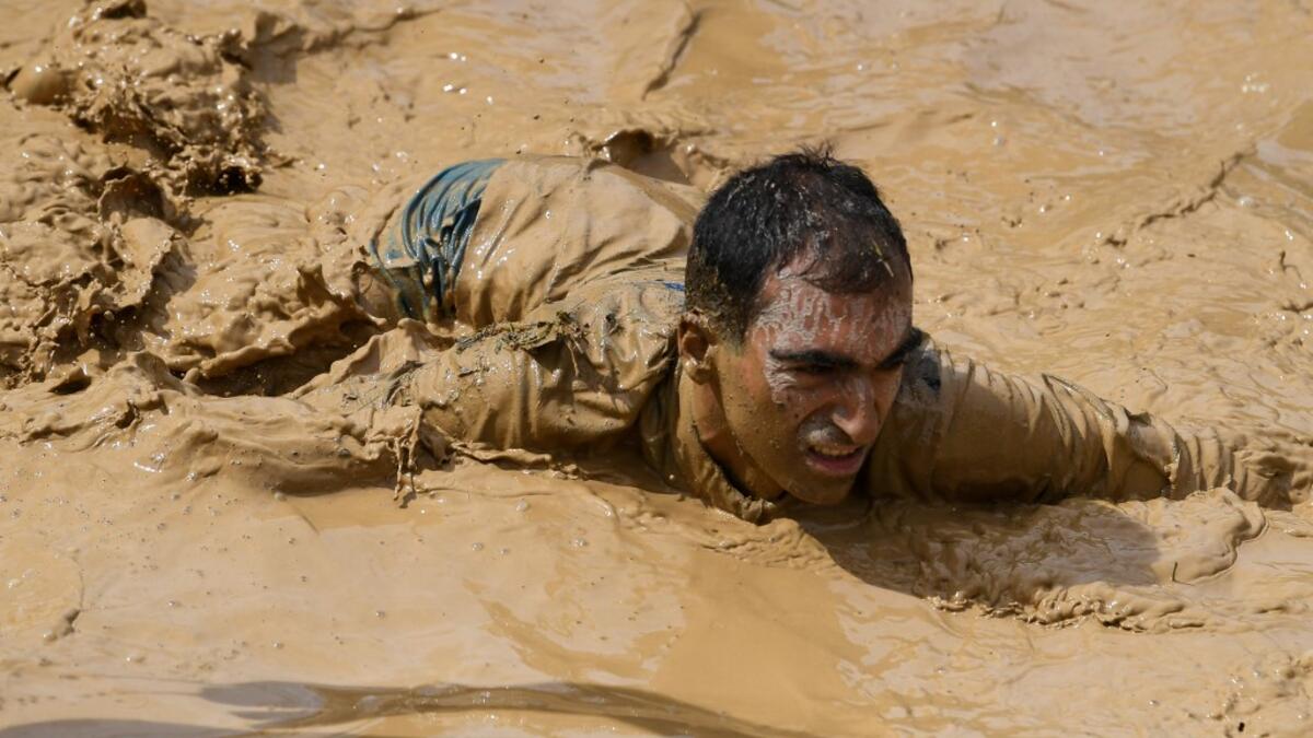 A runner crawls in mud as he takes part in the Mud Day, a 13km race with obstacles in Beynes, near Paris on June 16, 2019.  ALAIN JOCARD / AFP